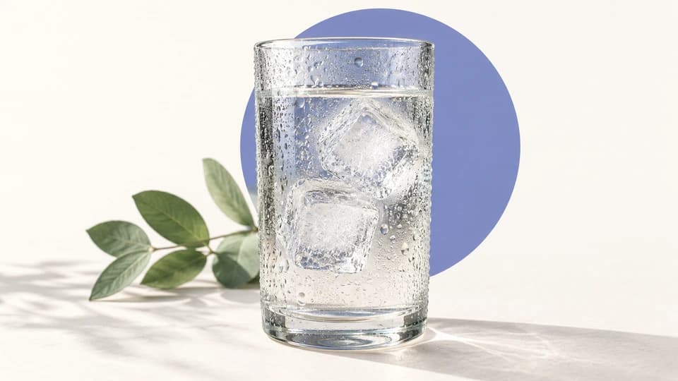 Vaso con agua fría y gotas de condensación en una composición editorial morada